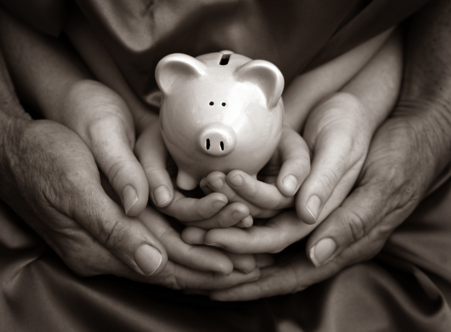 Black and white photo of 3 sets of hands stacked on top of each other from largest to smallest holding a piggy bank